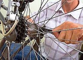 Rad mit Nabe und Speichen im Vordergrund, eine Person mit Maulschlüssel in der Hand schraubt am Zahnkranz.