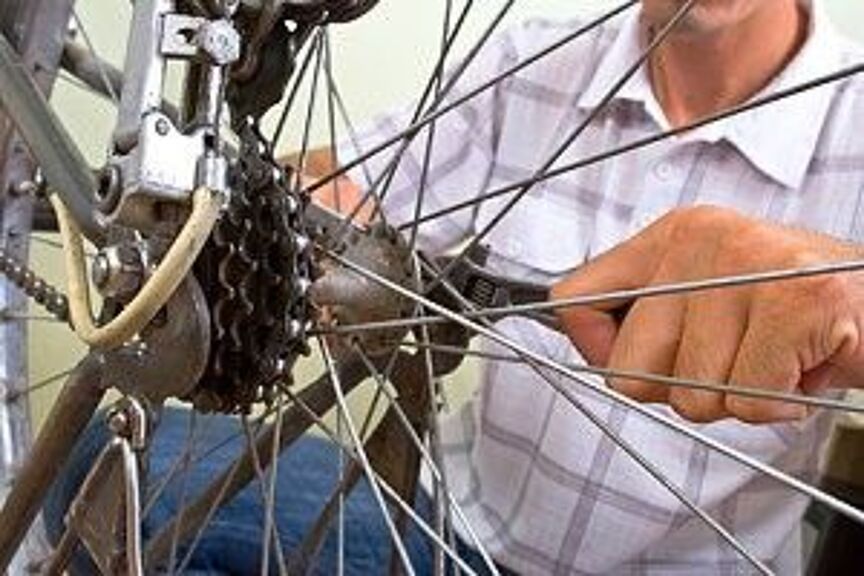 Rad mit Nabe und Speichen im Vordergrund, eine Person mit Maulschlüssel in der Hand schraubt am Zahnkranz.